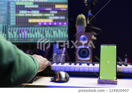 African american musician working on editing new music with a greenscreen, operating on mixing console and stereo gear in home studio. Skilled audio engineer improving sound quality. African american musician working on editing new music with a greenscreen, operating on mixing console and stereo gear in home studio. Skilled audio engineer improving sound quality. 124920407