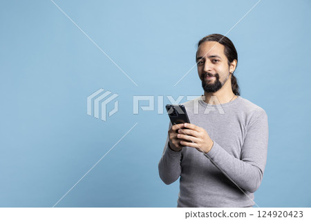 Professional young man in casual clothes using a phone with a pensive expression, embodying the modern digital professionalism. Cool male model uses device on blue background. 124920423