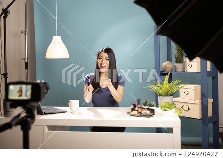Cheerful cosmetics content creator filming a lipstick brand review, using a professional setup with studio lighting. Ideal for digital advertising, influencer marketing, and social media trends. Cheerful cosmetics content creator filming a lipstick brand review, using a professional setup with studio lighting. Ideal for digital advertising, influencer marketing, and social media trends. 124920427