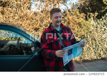 Car, reading map and travel on vacation, road trip and planning holiday for navigation. Young Caucasian man in stylish clothes reading a map standing near a car Car, reading map and travel on vacation, road trip and planning holiday for navigation. Young Caucasian man in stylish clothes reading a map standing near a car 124920725