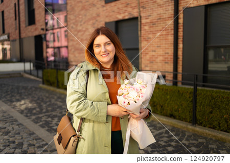 Happy woman holding flowers in a modern urban setting, smiling outdoors 124920797