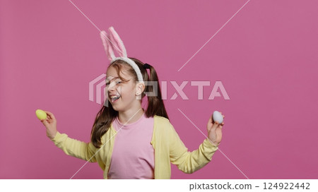 Adorable little girl playing peek a boo game in studio, showing her handcrafted colored easter eggs against pink background. Cheerful playful kid with bunny ears fooling around. Camera A. Adorable little girl playing peek a boo game in studio, showing her handcrafted colored easter eggs against pink background. Cheerful playful kid with bunny ears fooling around. Camera A. 124922442