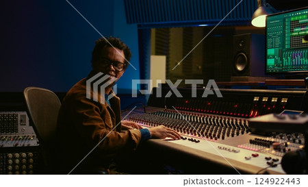 Music producer operating mixing console in control room and working with audio recording software on pc, post production. Sound engineer editing tracks to produce new songs. Camera B. Music producer operating mixing console in control room and working with audio recording software on pc, post production. Sound engineer editing tracks to produce new songs. Camera B. 124922443