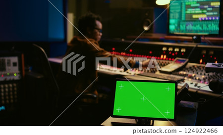African american tracking engineer works with greenscreen, operates audio console with moving faders and colored meters. Specialist pressing buttons and faders to edit audio recordings. Camera B. African american tracking engineer works with greenscreen, operates audio console with moving faders and colored meters. Specialist pressing buttons and faders to edit audio recordings. Camera B. 124922466