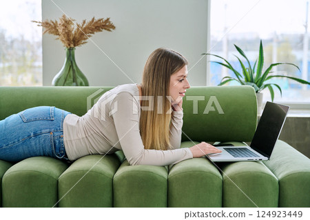 Young woman lying on sofa at home using laptop Young woman lying on sofa at home using laptop 124923449