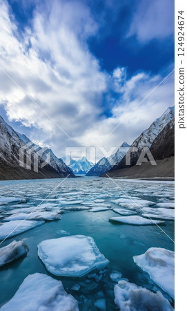 Majestic Frozen Lake with Turquoise Waters Surrounded by Dark Rocky Mountains Under Dramatic Sky 124924674