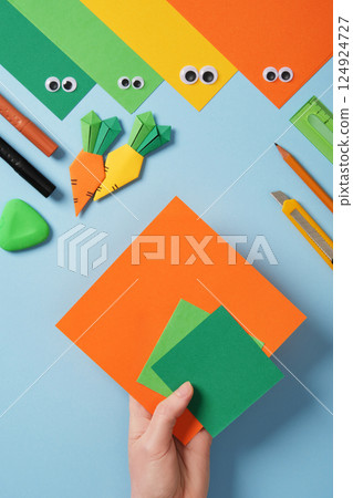 Making origami carrot. DIY project. Take a square sheet of orange color and two small squares of green color. Making origami carrot. DIY project. Take a square sheet of orange color and two small squares of green color. 124924727