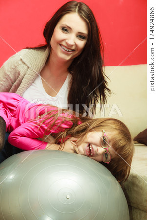 Mother sitting on exercise ball with daughter Mother sitting on exercise ball with daughter 124924866