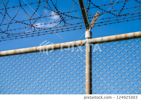 Barbed wire fence symbolizing border control, geopolitical tensions, and restricted freedoms in modern society. Barbed wire border security fence. Barrier border. Boundary security wall. Private area. Barbed wire fence symbolizing border control, geopolitical tensions, and restricted freedoms in modern society. Barbed wire border security fence. Barrier border. Boundary security wall. Private area. 124925883