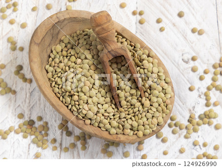 Bowl full of dried raw green lentils with a wooden scoop on white table top view. Vegetarian food 124926990