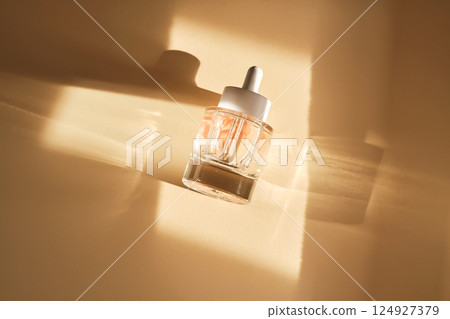 A bottle of luxury serum with petals on a beige background. 124927379