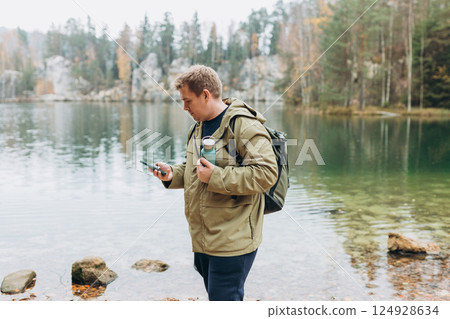 Travel backpacker standing with phone near the majestic lake. Travel, adventure. Concept of an active lifestyle. High quality photo Travel backpacker standing with phone near the majestic lake. Travel, adventure. Concept of an active lifestyle. High quality photo 124928634