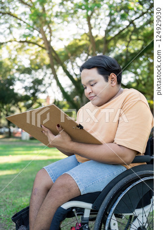 Young Person in Wheelchair Enjoying Outdoor Activities in a Park on a Sunny Day with Green Trees and Grass 124929030