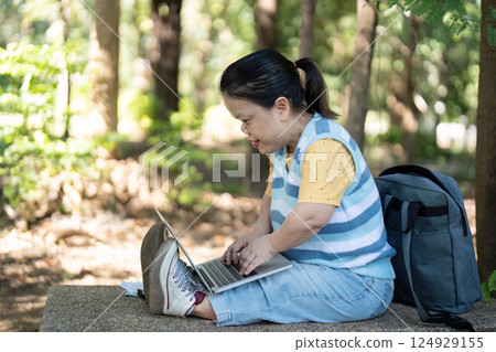 Person with Achondroplasia Using Laptop Outdoors in a Park Setting, Embracing Technology and Nature 124929155