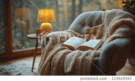 An inviting armchair with a book and warm blanket offers a cozy reading spot. An inviting armchair with a book and warm blanket offers a cozy reading spot. 124929567