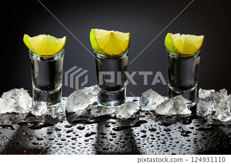 Tequila shots with lime slices on a wet black table. Tequila shots with lime slices on a wet black table. 124931110