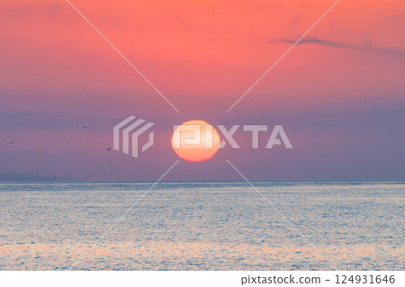 Sunrise view from Malaga seaside city in Andalusia, Spain, Europe. Serene sunrise over calm ocean waters. Large, vibrant sun descends below the horizon, painting the sky in hues of pink and purple. 124931646