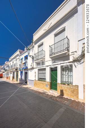 Nerja town, a resort of The Costa del Sol seaside region in Andalusia in the south of Spain. Sunny street scene with whitewashed houses and balconies. Cobblestone street and clear blue sky. 124931678