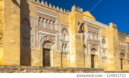 The Mosque Cathedral of Cordoba, Cathedral of Our Lady of the Assumption in Cordoba town in Spain. Ornate facade of a historic building, showcasing stonework and arched doorways under a blue sky. The Mosque Cathedral of Cordoba, Cathedral of Our Lady of the Assumption in Cordoba town in Spain. Ornate facade of a historic building, showcasing stonework and arched doorways under a blue sky. 124931712