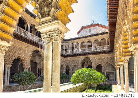 The Alcazar of Seville, historic royal palace in Seville town, Andalusia, Spain. Ornate courtyard with intricate arches and columns, showcasing detailed stonework and lush greenery. The Alcazar of Seville, historic royal palace in Seville town, Andalusia, Spain. Ornate courtyard with intricate arches and columns, showcasing detailed stonework and lush greenery. 124931715