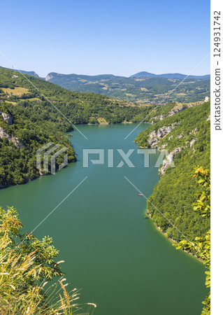 A canyon on the Vrbas River in Bosnia and Herzegovina, Europe. Scenic river bend winds through lush green hills, framed by clear blue skies and distant mountains. Serene landscape, perfect for escape. 124931742