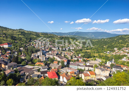 Jajce town in Bosnia and Herzegovina, Europe. Scenic town nestled in valley with mountains in the background under a sunny sky with white clouds and lush green trees surrounding the buildings 124931752