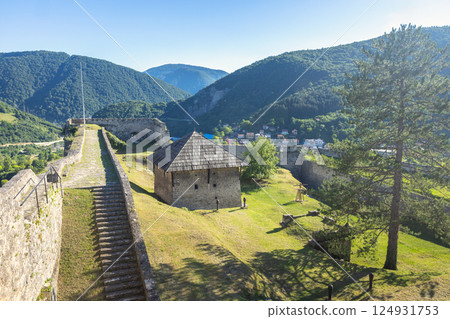 Walled City of Jajce, medieval fortress in Jajce town in Bosnia and Herzegovina, Europe. Historic fortress on green hill, overlooking a valley and mountains on a bright, sunny day with a blue sky. 124931753