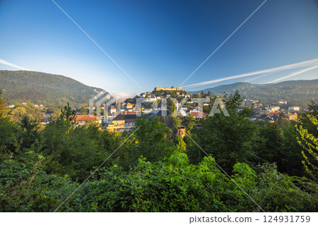 Jajce town in Bosnia and Herzegovina, Europe. Hilltop Settlement: A scenic view of a European town nestled in a valley, crowned by a historic fortress under a blue sky. 124931759