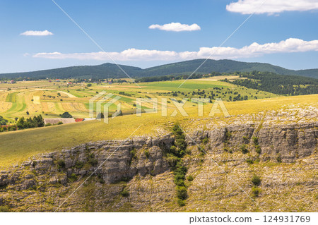 View of country in Bosnia and Herzegovina, Europe. Scenic vista: rolling hills, meadows, and distant mountains beneath a blue sky with fluffy clouds on a bright sunny day in the countryside. 124931769