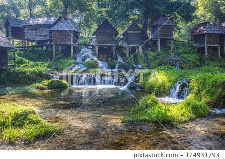 The Mlincici wooden watermills at Pliva river near Jajce town in Bosnia and Herzegovina, Europe. Historic watermills stand along a cascading stream, lush with greenery. The Mlincici wooden watermills at Pliva river near Jajce town in Bosnia and Herzegovina, Europe. Historic watermills stand along a cascading stream, lush with greenery. 124931793