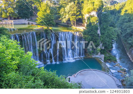The Pliva Waterfall in Jajce town, Bosnia and Herzegovina, Europe. Idyllic waterfalls cascading into a turquoise pool surrounded by lush greenery, offering a serene escape into nature's beauty. 124931803