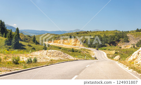 Road in Bosnia and Herzegovina, Europe. Scenic road winding through green hills beneath a clear blue sky, promising a journey filled with natural beauty and adventure. 124931807