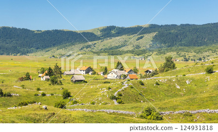 View of country in Bosnia and Herzegovina, Europe. Scenic landscape featuring a small village nestled amidst rolling green hills and a mountain backdrop under a clear blue sky. View of country in Bosnia and Herzegovina, Europe. Scenic landscape featuring a small village nestled amidst rolling green hills and a mountain backdrop under a clear blue sky. 124931818