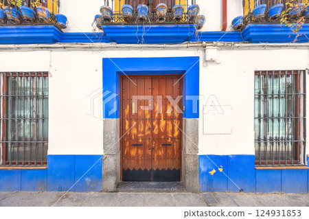 Cordoba town in Spain. Traditional building facade with blue trim, wooden door, and iron window grilles. A classic architectural detail. Cordoba town in Spain. Traditional building facade with blue trim, wooden door, and iron window grilles. A classic architectural detail. 124931853