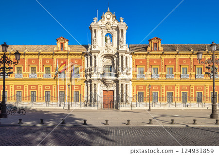The Palace of San Telmo in Seville town, capital of Andalusia in Spain. Grand palace facade with ornate details, under a bright blue sky. Flags fly proudly. 124931859