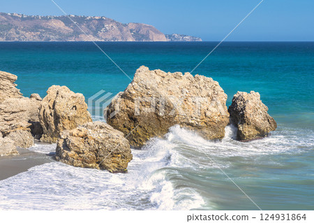 Nerja town, a resort of The Costa del Sol seaside region in Andalusia in the south of Spain. Ocean waves crashing against coastal rocks, a scenic view of turquoise water and distant mountains. Nerja town, a resort of The Costa del Sol seaside region in Andalusia in the south of Spain. Ocean waves crashing against coastal rocks, a scenic view of turquoise water and distant mountains. 124931864