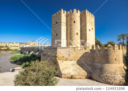 The Calahorra Tower on a one side of the Roman Bridge in Cordoba town in Spain. Ancient stone tower and bridge overlooking a river. Historic architecture under a clear blue sky. The Calahorra Tower on a one side of the Roman Bridge in Cordoba town in Spain. Ancient stone tower and bridge overlooking a river. Historic architecture under a clear blue sky. 124931896