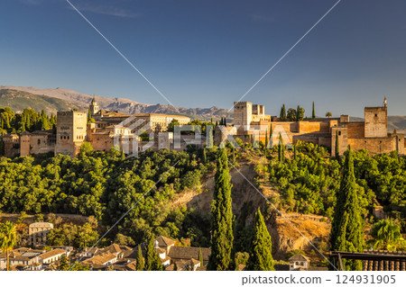 Panorama of the Alhambra from the Mirador de San Nicolas viewpoint in Granada town in Spain at sunset. Ancient castle on a hilltop overlooking a town, bathed in golden sunlight. 124931905