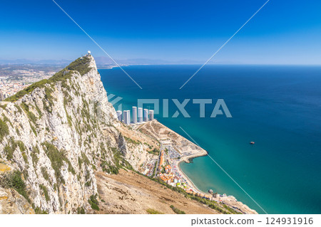 Gibraltar, British Overseas Territory and city on the Iberian Peninsula. Coastal cliffs and ocean view. Serene landscape with buildings and a clear blue sky. Gibraltar, British Overseas Territory and city on the Iberian Peninsula. Coastal cliffs and ocean view. Serene landscape with buildings and a clear blue sky. 124931916