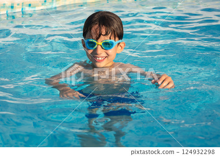 Child wearing swimming goggles swim in a pool on a sunny day. 124932298