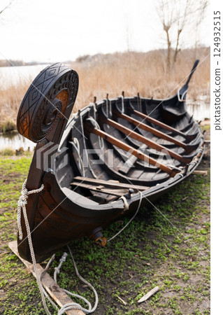 A meticulously crafted wooden Viking longship rests on the grass near a lake, showcasing intricate carvings and traditional construction A meticulously crafted wooden Viking longship rests on the grass near a lake, showcasing intricate carvings and traditional construction 124932515