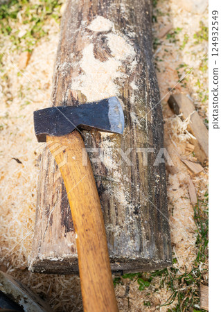 A weathered axe with a wooden handle rests on a freshly cut log, surrounded by wood shavings 124932549