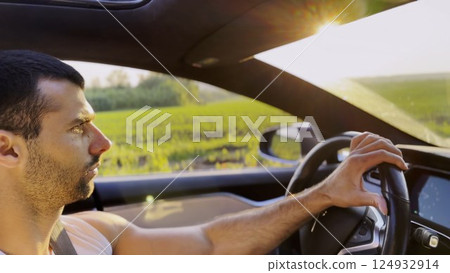 Profile of young handsome man driving a modern electric car with sunlight at background. Young male driver riding on electrical vehicle at countryside. Concept of journey and trip. Close up 124932914