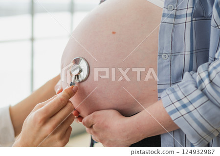 Doctor examining pregnant woman holding stethoscope near big belly listening baby heartbeat. Gynecologist doctor consulting patient about pregnancy in hospital office. Visit to doctor medical checkup Doctor examining pregnant woman holding stethoscope near big belly listening baby heartbeat. Gynecologist doctor consulting patient about pregnancy in hospital office. Visit to doctor medical checkup 124932987