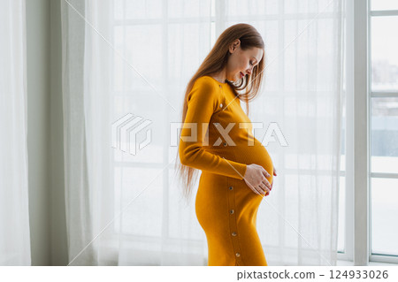 Pregnancy motherhood people expectation future. Pregnant woman with big belly standing near window at home. Girl hugging her tummy enjoying pregnancy. Maternity tenderness parenthood new life concept Pregnancy motherhood people expectation future. Pregnant woman with big belly standing near window at home. Girl hugging her tummy enjoying pregnancy. Maternity tenderness parenthood new life concept 124933026