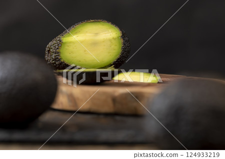 sliced small avocado with soft overripe flesh on a wooden board, side view sliced small avocado with soft overripe flesh on a wooden board, side view 124933219
