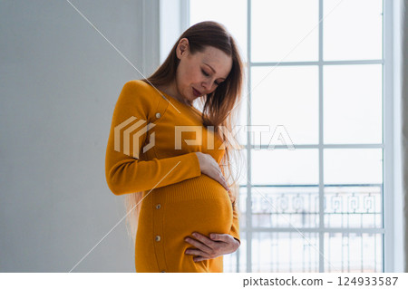 Pregnancy motherhood people expectation future. Pregnant woman with big belly standing near window at home. Girl hugging her tummy enjoying pregnancy. Maternity tenderness parenthood new life concept Pregnancy motherhood people expectation future. Pregnant woman with big belly standing near window at home. Girl hugging her tummy enjoying pregnancy. Maternity tenderness parenthood new life concept 124933587
