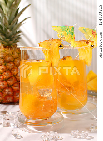 Cold homemade cocktail or lemonade with pineapple, orange, ice on sunny kitchen modern table, Detox diet and summer party concept. Refreshing summer diet drink recipe, restaurant menu 124933815