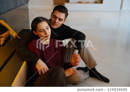 Couple enjoying a cozy moment by a modern fireplace in a stylish interior Couple enjoying a cozy moment by a modern fireplace in a stylish interior 124934099