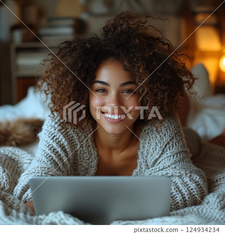Young Woman Smiling While Using Laptop in a Cozy Evening Setting 124934234